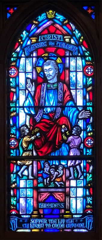 A stained glass window depicting Jesus and children at The Church of the Holy Comforter.